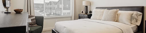 A bedroom with a large bed and a window with blinds.