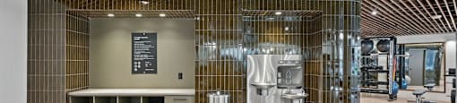 A gym storage wall area with a water fountain and bench.