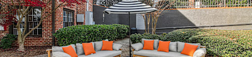 Two orange cushions on a grey sofa in a courtyard.