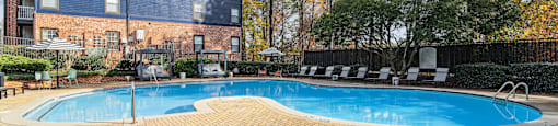 A swimming pool surrounded by a brick patio and a brick building in the background.