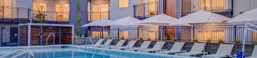 A large swimming pool in front of a modern building with sun loungers.