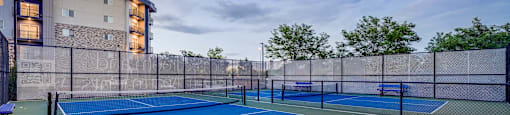 A tennis court is surrounded by a fence and a building.