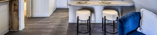 A kitchen with white cabinets and a dining table with two stools.
