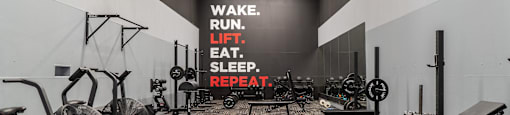 a workout room with weights and cardio machines and a motivational wall in the background