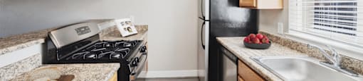A kitchen with a black refrigerator, a stove, and a counter with a cutting board on it.