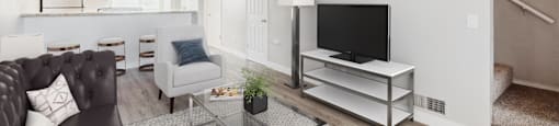 A living room with a grey couch, a glass coffee table, and a television on a stand.