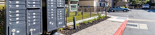 Two black mailboxes on a brick sidewalk in front of a residential street.
