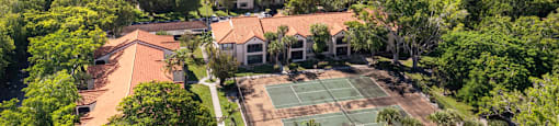 A tennis court is surrounded by trees and buildings in the distance.
