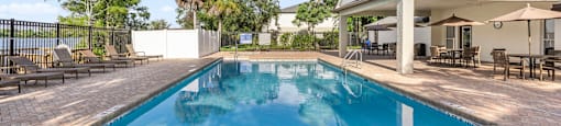 A pool surrounded by a brick patio and a house in the background. at Cascades at Clear Lake Apartments, Florida