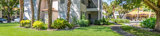 A white building with a balcony is surrounded by trees and green grass.