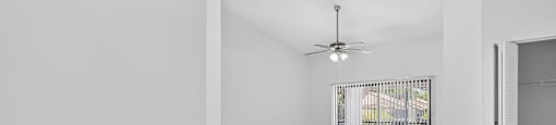 A room with a ceiling fan and sliding glass doors.