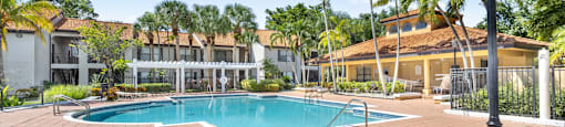 A pool surrounded by a brick patio and palm trees.