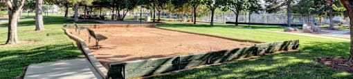 A baseball field is surrounded by trees and has a concrete walkway.