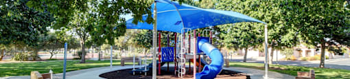 A playground with a blue canopy and a slide.
