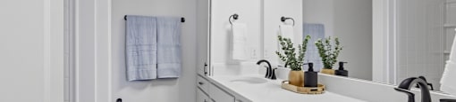 A white bathroom with a sink, mirror, and a towel hanging on the wall.
