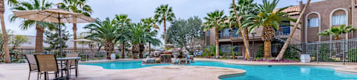 A pool surrounded by palm trees and a building in the background.