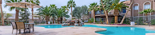 A pool surrounded by palm trees and a building in the background.