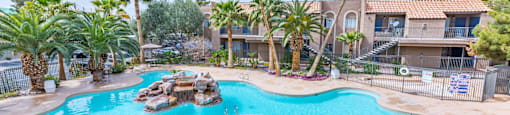 A large swimming pool surrounded by palm trees and a few other trees.