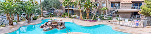 A large swimming pool surrounded by palm trees and a patio area with chairs and umbrellas.