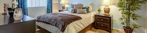 A bedroom with a bed, nightstand, and a potted plant.