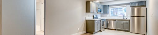 A kitchen with a refrigerator, microwave, and oven is visible from a living room.