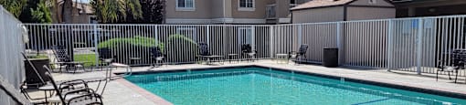 A pool surrounded by a fence with chairs around it.