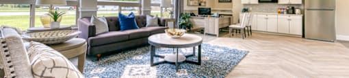 A well-lit, spacious living room with a grey sofa, a round coffee table, and a large window.