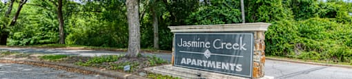 A sign for Jasmine Creek Apartments is displayed in front of a tree.