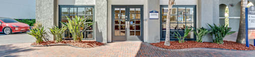 the front entrance of a building with a brick sidewalk and palm trees