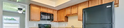 A black refrigerator is in a kitchen with wooden cabinets at Westminster Chase Apartments, Tampa, Florida