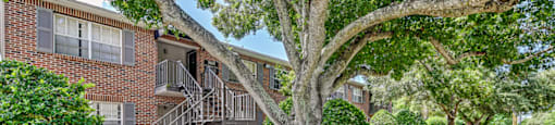 A tree in front of a brick building with a metal staircase. at Green Oaks Apartments, Tampa