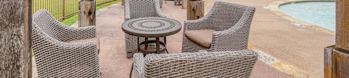 A patio with chairs and a table is covered by a wooden roof.