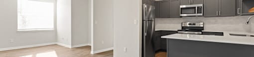 an empty living room with a kitchen with stainless steel appliances at Switchback on Platte Apartments, Littleton, CO 80120