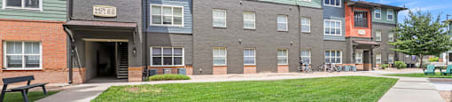 a sidewalk in front of an apartment building with a lawn at Switchback on Platte Apartments, Littleton, CO