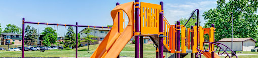 a playground with a yellow slide and other playground equipment at Willow Hill Apartments, Justice, IL