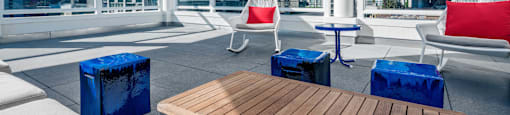A wooden table is in the middle of a patio with white chairs and umbrellas. at G12 Apartments, Los Angeles, CA