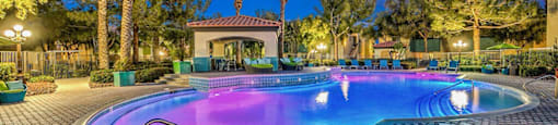 a large swimming pool at night with palm trees at Mirasol Apartments, Las Vegas