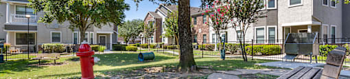 a park with a red fire hydrant and benches in front of an apartment building at Sladestone Shadow Creek, Texas