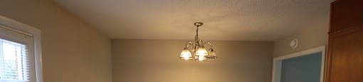 A room with a brown floor and a chandelier hanging from the ceiling.
