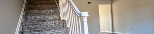 A staircase with a grey carpeted runner and white handrail.