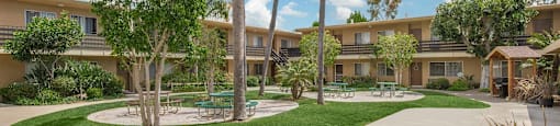 a courtyard with palm trees and a sidewalk in front of a building at Villa La Paz Apartments, California, 90706