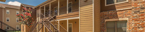 A sunny day at a brick apartment complex with a red flower in bloom at The Villages at Lost Creek Apartments, San Antonio, TX, 78247