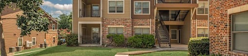 A large apartment complex with a green lawn in front at The Villages at Lost Creek Apartments, Texas