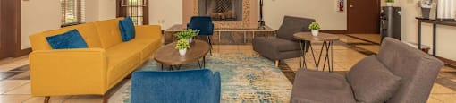 A living room with a yellow couch, blue chair, and a fireplace at The Villages at Lost Creek Apartments, San Antonio