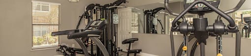 A spacious home gym with a treadmill, elliptical trainer, and a bench at The Villages at Lost Creek Apartments, San Antonio, 78247