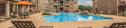 A pool surrounded by chairs and umbrellas in front of apartment buildings at The Villages at Lost Creek Apartments, San Antonio