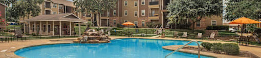 A large swimming pool surrounded by a fence and trees with apartment buildings in the background at The Villages at Lost Creek Apartments, Texas, 78247