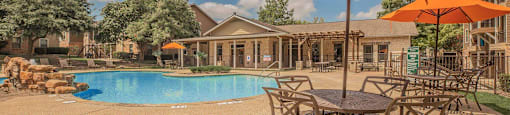 A large orange umbrella is in the foreground of a pool area at The Villages at Lost Creek Apartments, San Antonio, TX, 78247