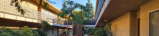 a hallway with potted plants and flowers outside of a building at Villa La Paz Apartments, California, 90706