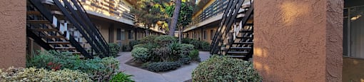 a courtyard between two buildings with plants and stairs at Villa La Paz Apartments, California, 90706